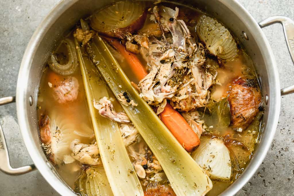 A stockpot full of chicken bones, vegetables and herbs cooked together to make homemade chicken stock.