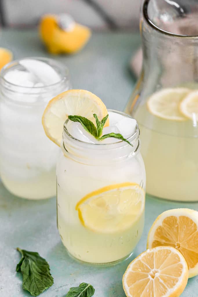 A glass of lemonade with ice and a lemon slice on top.