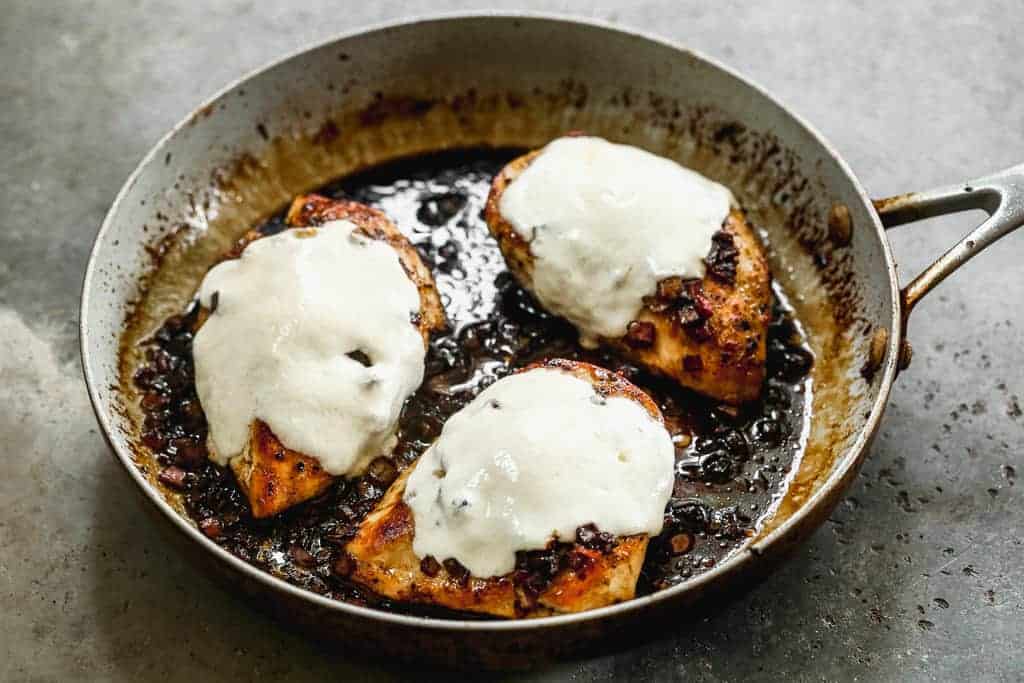 Chicken breasts in a skillet, with melted mozzarella cheese on top.