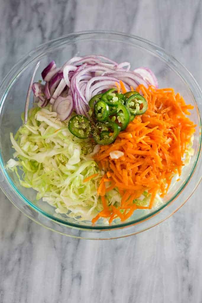 A large glass bowl with finely shredded cabbage, carrot, onion, jalapeno and oregano.