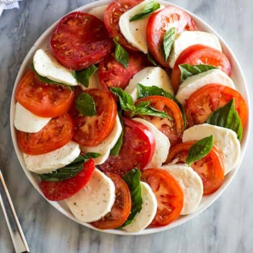 tomatoes, cucumbers, and mozzarella fanned out in a circle on a white plate.