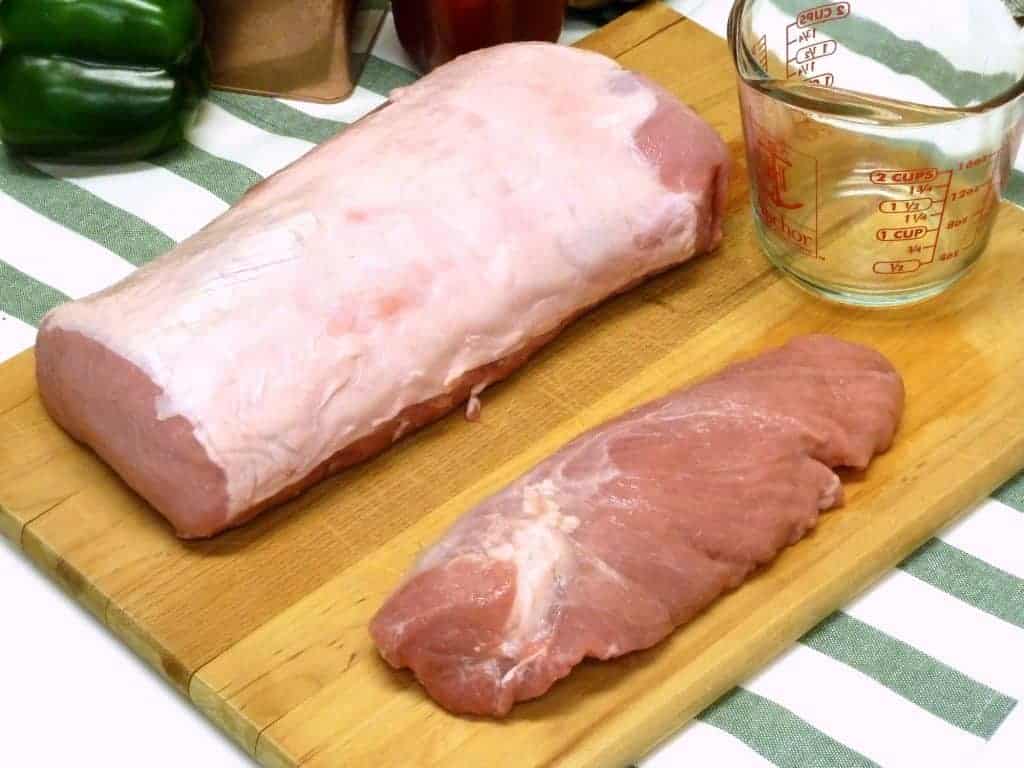 A large piece of pork loin and pork tenderloin on a cutting board side by side.