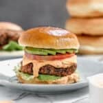 Black bean burger served in a hamburger bun topped with sauce, tomato and avocado.