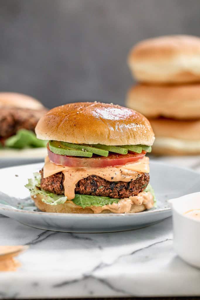 Black bean burger served in a hamburger bun topped with sauce, tomato and avocado.