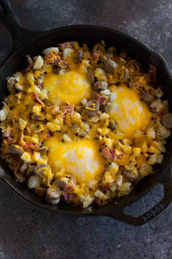 Breakfast hash with three eggs baked on top, served in a cast iron skillet.