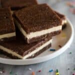 Homemade brownie ice cream sandwich squares stacked on a white plate with sprinkles on the side.