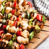 A wooden cutting board with easy Chicken Kabobs with marinated chicken, bell peppers, and onion. It's a simple grilled dish that only takes 10 minutes to prep!