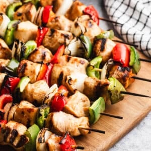 A wooden cutting board with easy Chicken Kabobs with marinated chicken, bell peppers, and onion. It's a simple grilled dish that only takes 10 minutes to prep!