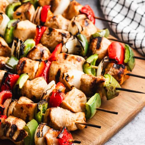 A wooden cutting board with easy Chicken Kabobs with marinated chicken, bell peppers, and onion. It's a simple grilled dish that only takes 10 minutes to prep!