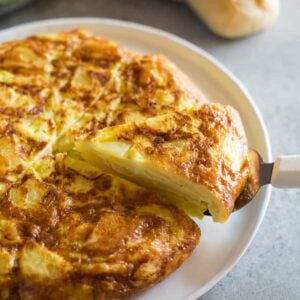 Spanish tortilla de patata on a plate with a slice being served and a baguette and salad in the background.