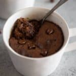 A white mug with chocolate cake baked in it and a spoon digging in for a bite.