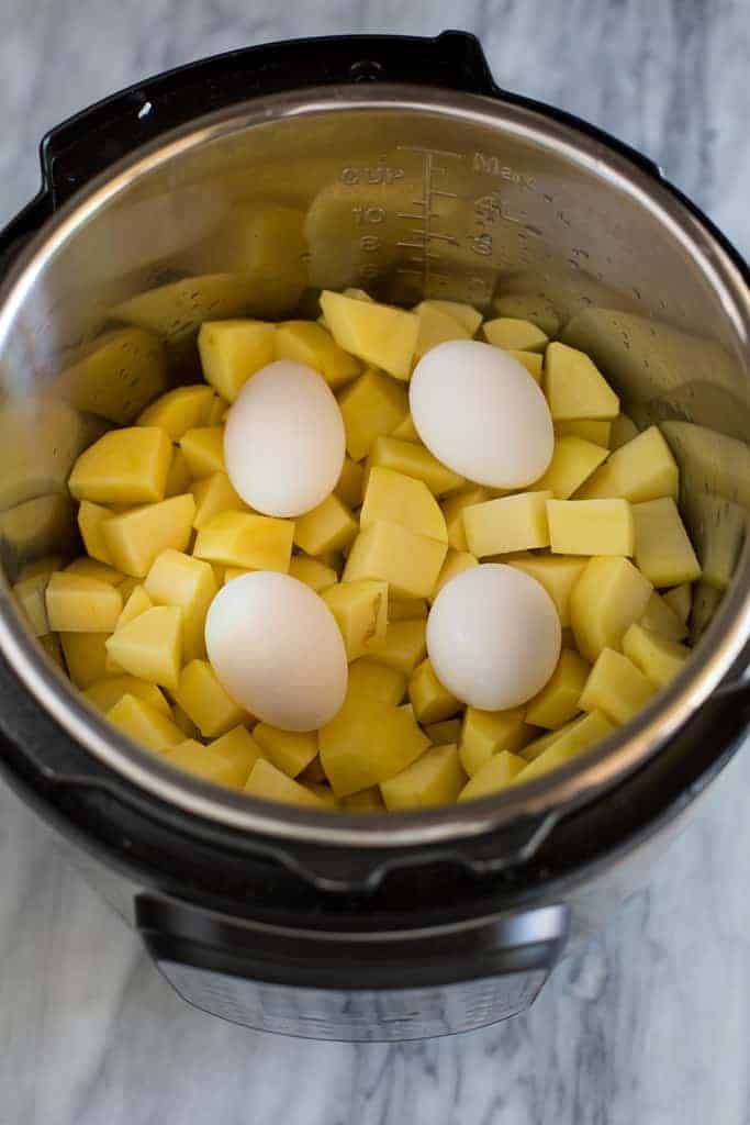 An instant pot with peeled and chopped potatoes and four eggs resting on top.