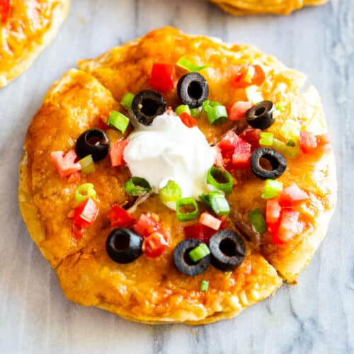 A homemade Mexican pizza topped with olives, tomatoes, green onions, and sour cream.