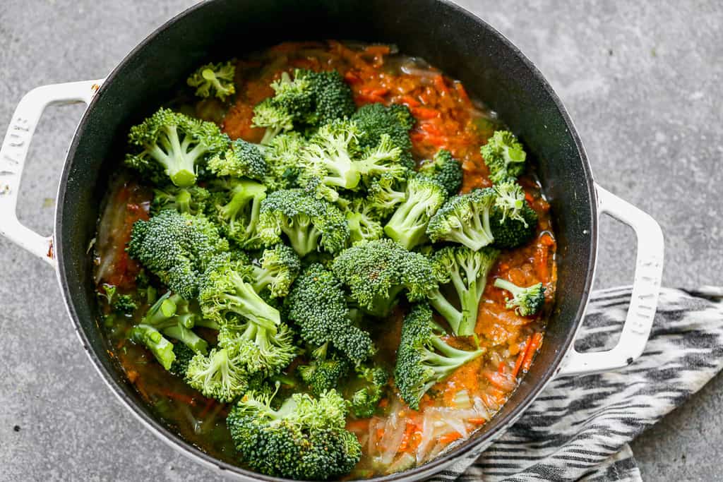 Fresh broccoli florets added to a soup pot with cooked veggies and broth.
