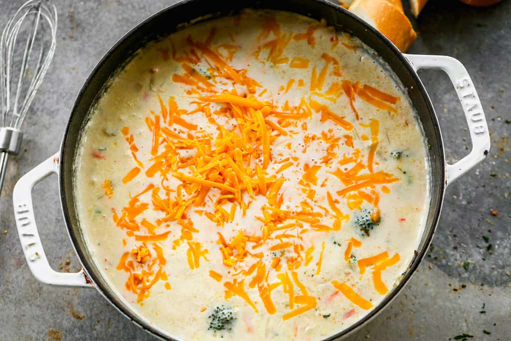 Freshly shredded cheddar cheese added to a pot of broccoli soup.