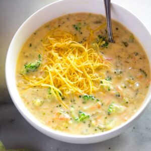 Broccoli cheese soup in a white bowl with shredded cheese on top and a spoon in it.