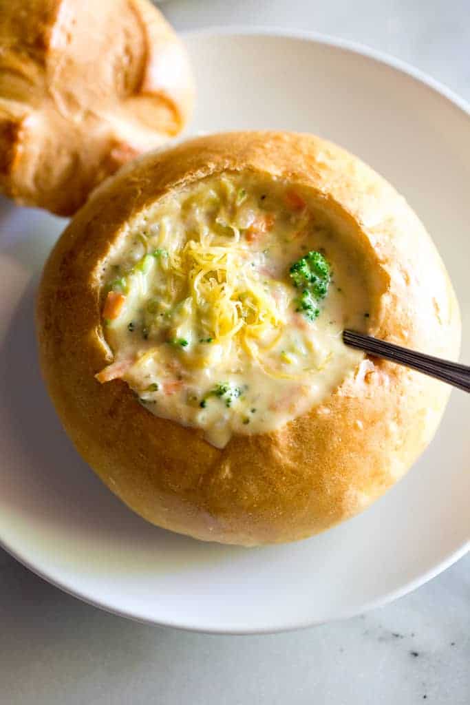 A bread bowl with broccoli cheese soup and a spoon in it.
