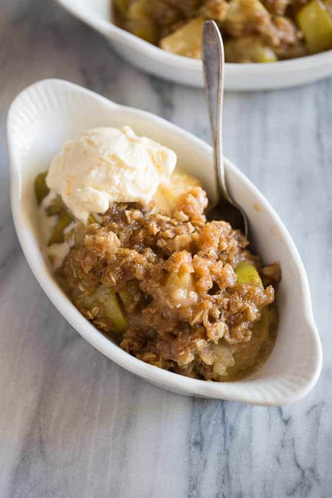 Individual size casserole dish with apple crisp in it topped with vanilla ice cream and a spoon.
