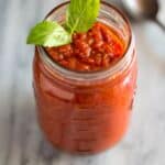 A mason jar full of homemade marinara with a basil leaf on top and spoon to the side.
