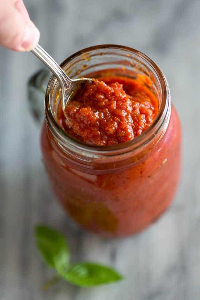Overhead view of a spoonful of marinara sauce being lifted from a mason jar.