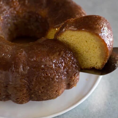 A rum cake bundt cake on a white plate with one slice being removed.