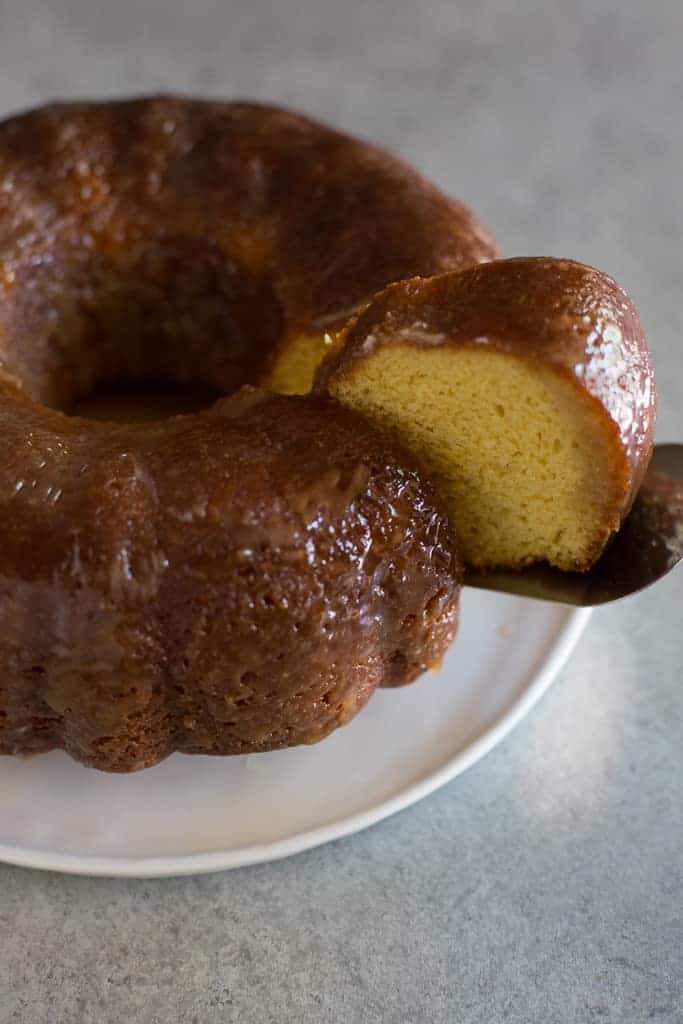 A rum cake bundt cake on a white plate with one slice being removed.