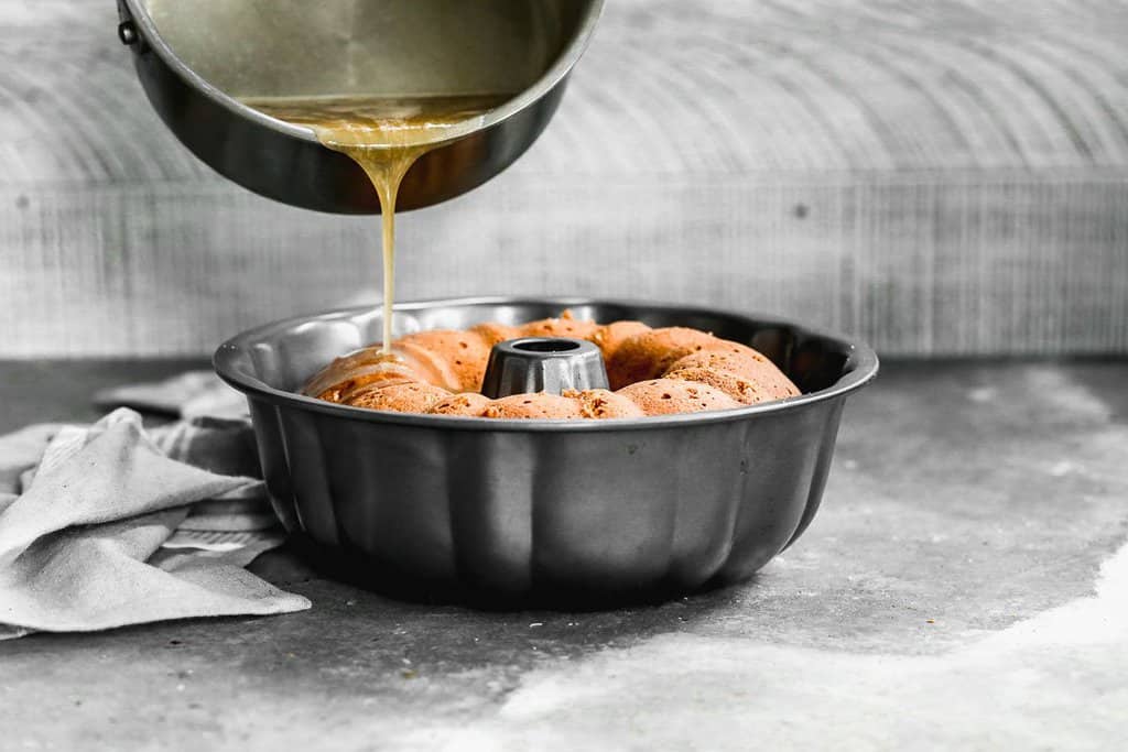 Warm butter rum glaze being poured over baked rum cake in a bundt pan.