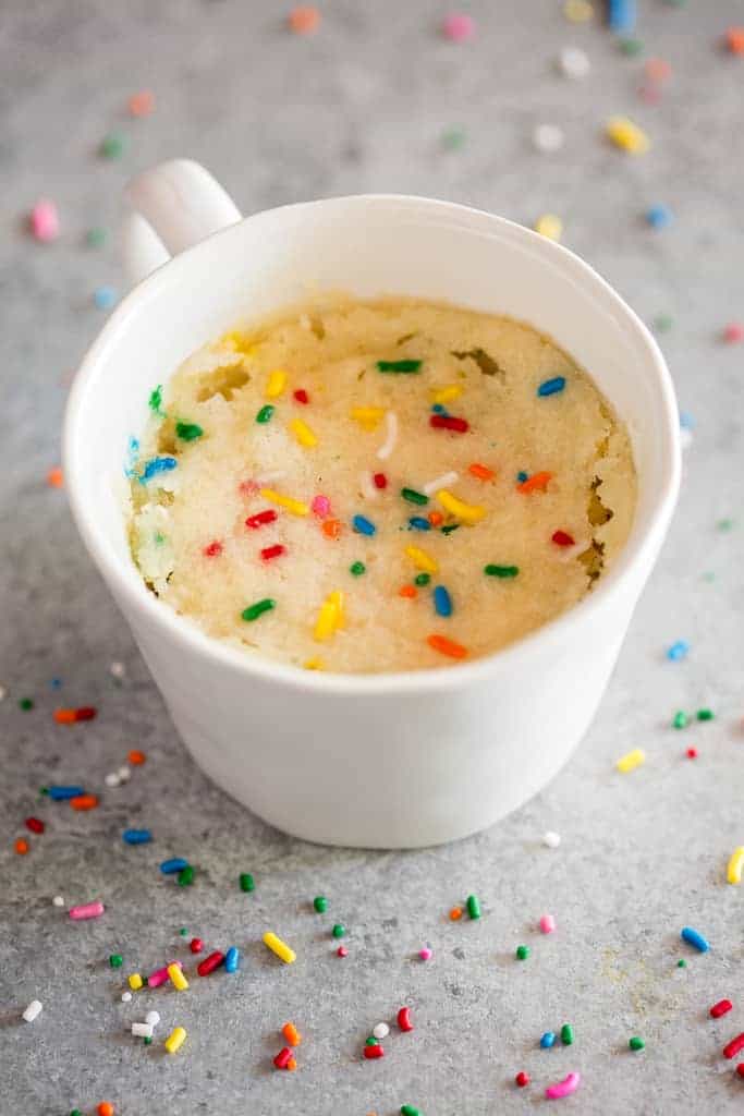 A mug with baked vanilla cake in it and sprinkles.
