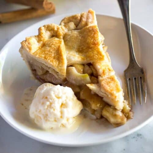 A slice of apple pie on a plate with a scoop of ice cream and a fork.