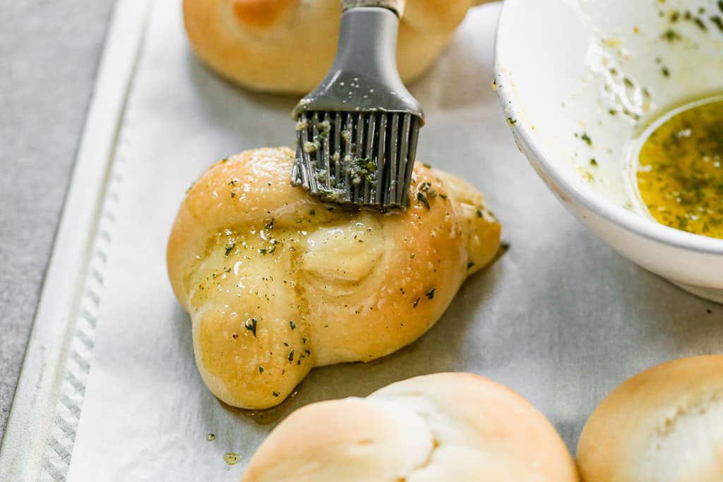 Baked bread knot being coated in garlic butter sauce.
