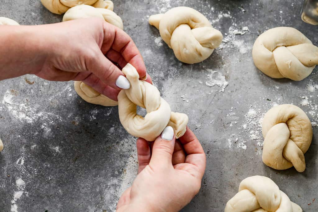 Hands forming a rope of bread dough into a knot.