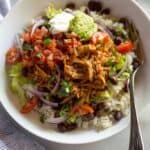 A white bowl with rice, black beans, sweet pork, salsa, guacamole and sour cream.