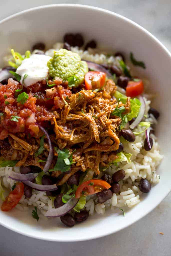 Close up photo of a sweet pork burrito bowl with rice and beans, salsa and guacamole.
