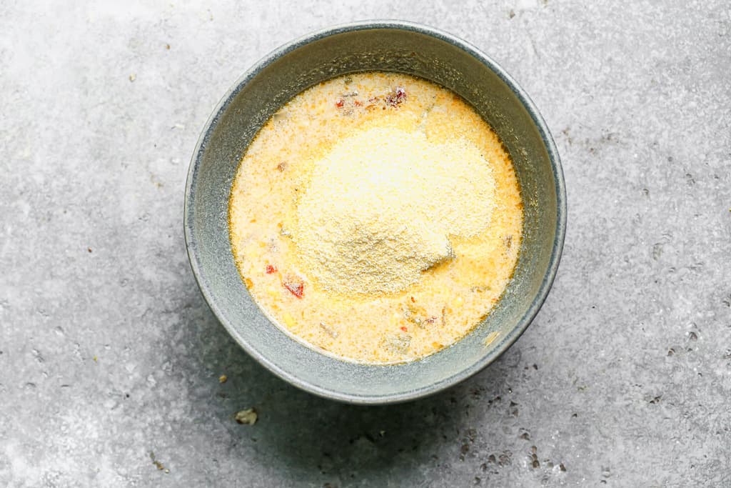 A bowl with soup broth in it, and cornmeal added on top, ready to stir in.