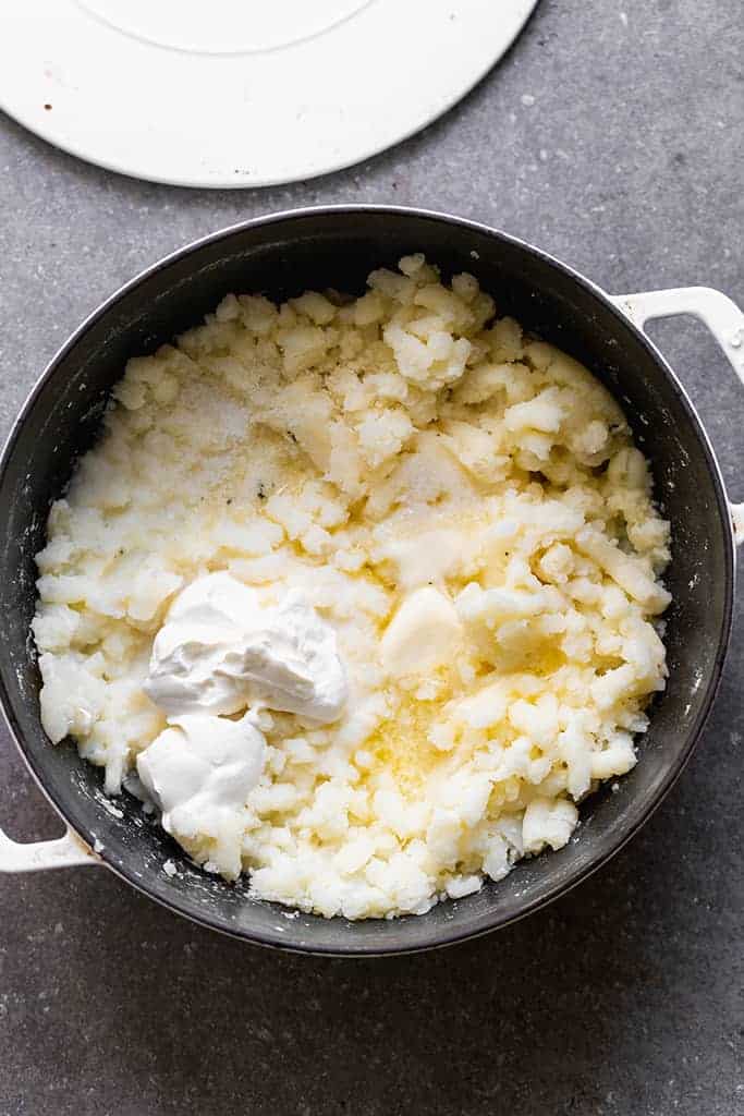 Lightly mashed potatoes in a saucepan with butter and sour cream added to mix in.
