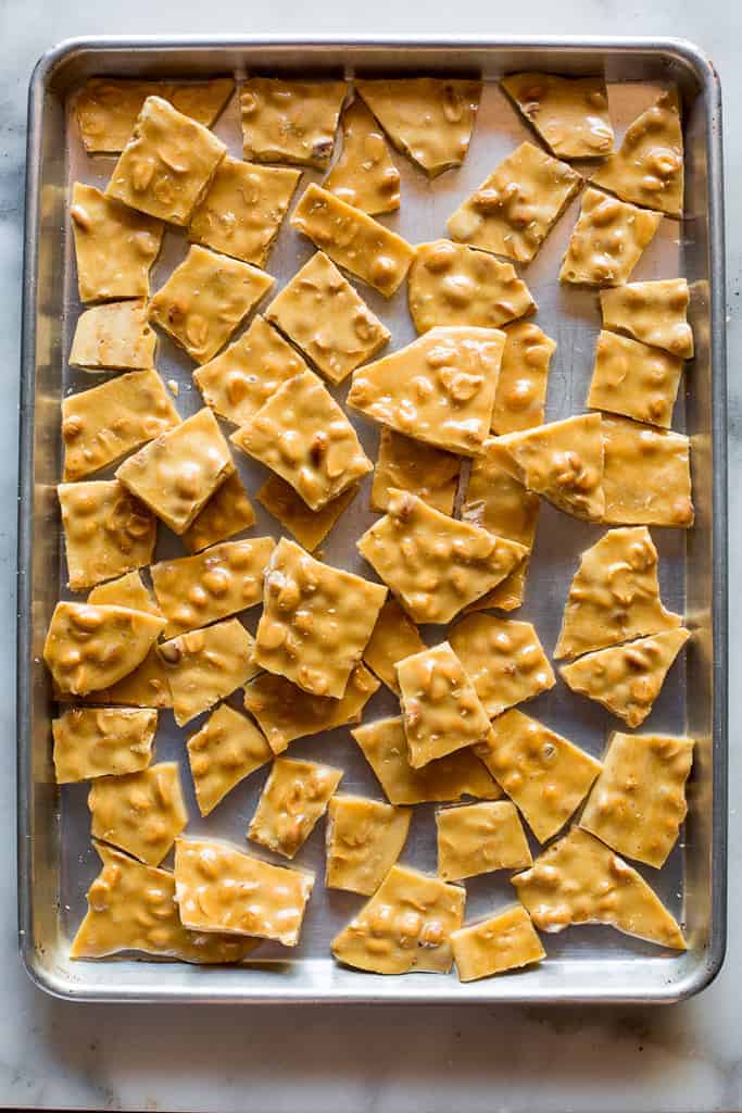 A baker's half sheet pan filled with broken up pieces of homemade peanut brittle.