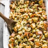 Homemade stuffing in a casserole dish with a wooden spoon.