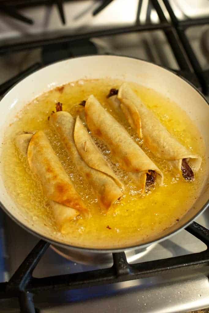 A skillet with taquitos frying in oil.