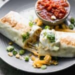 A breakfast burrito on a plate with salsa, sour cream and green onions on top.