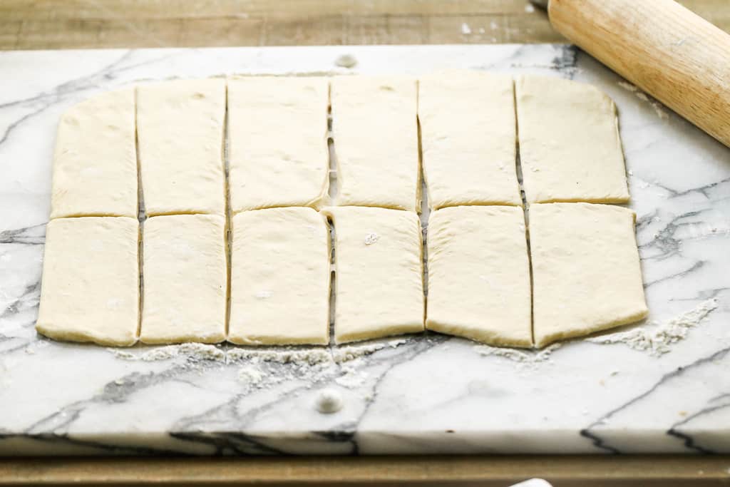 Rolled out bread dough cut into rectangles to shape dinner rolls.