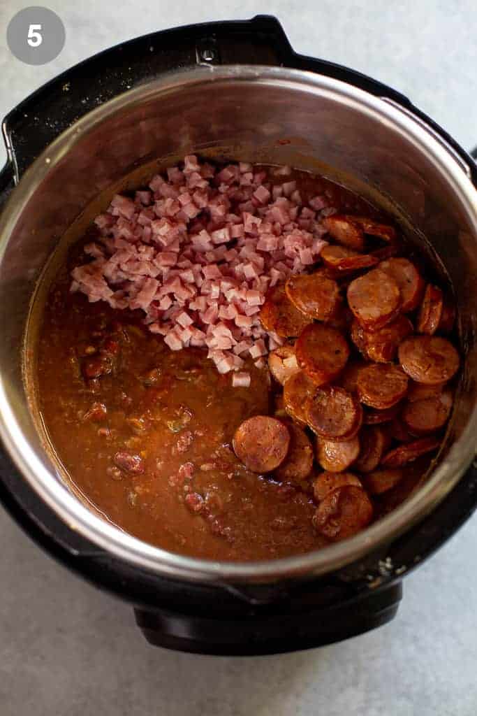 An instant pot with red beans and rice mixture, chopped ham and sausage on top.