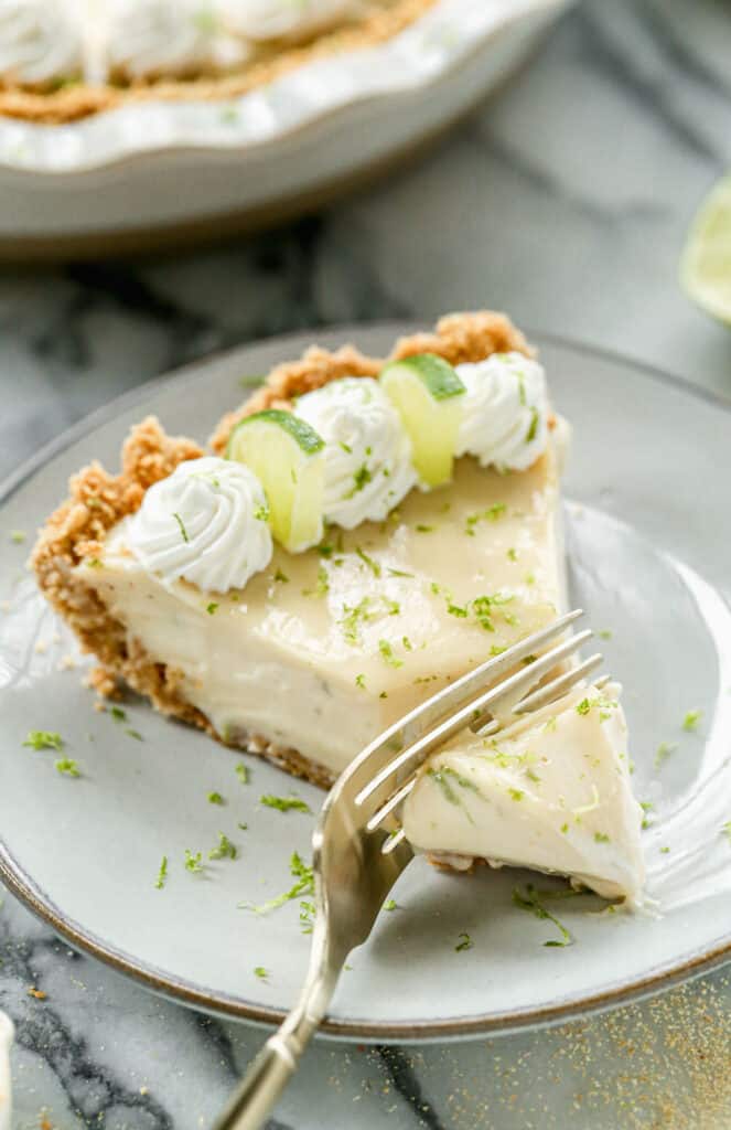 A slice of key lime pie on a plate with a fork removing a bite.