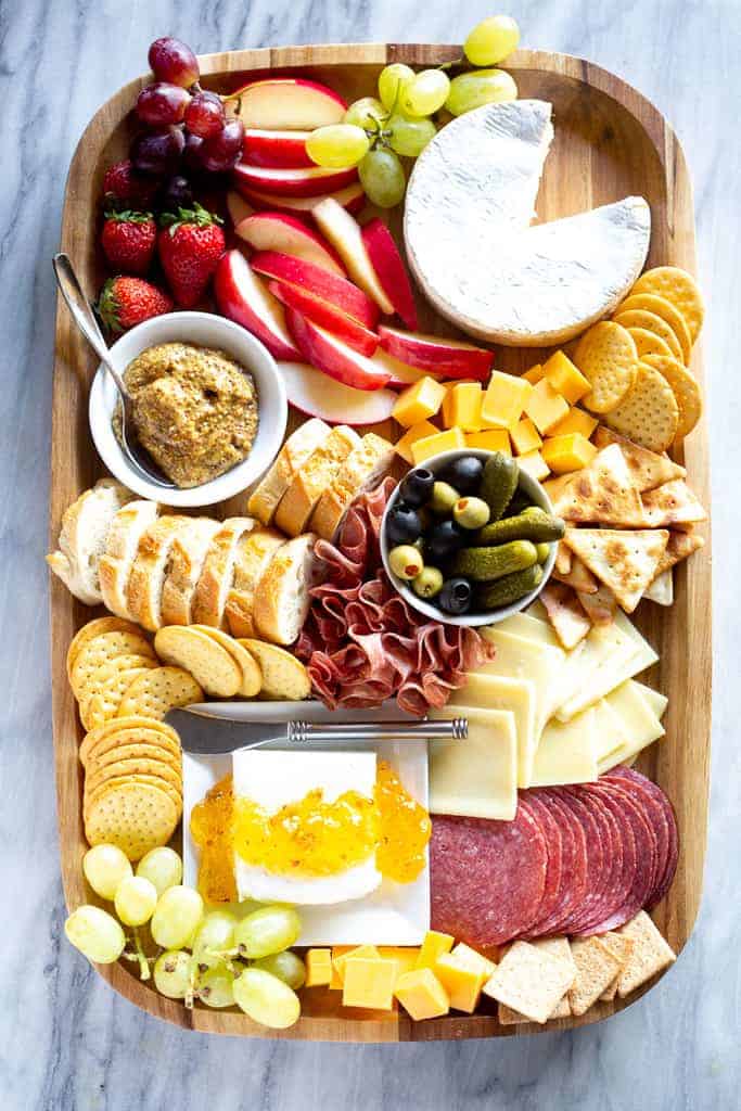Planche de charcuterie avec viandes, fromages tranchés, trempettes, craquelins et fruits, servis sur une planche de bois.