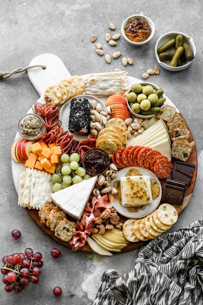 A large round charcuterie board with meats, cheese, fruits, nuts and crackers.