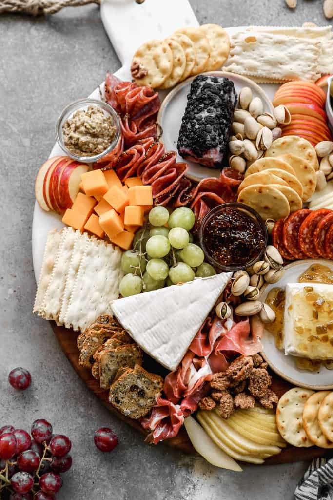 A complete meat and cheese board with gaps filled in with nuts, fruit, and chocolate.