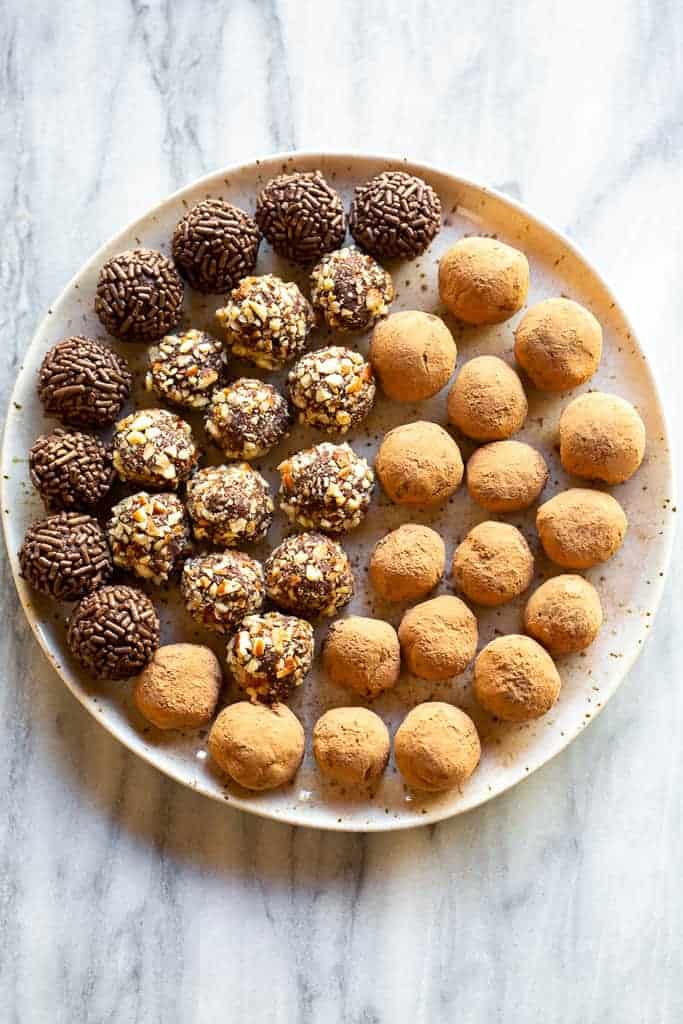 Overhead view of a plate with truffles coated in cocoa powder, chopped nuts, and sprinkles.