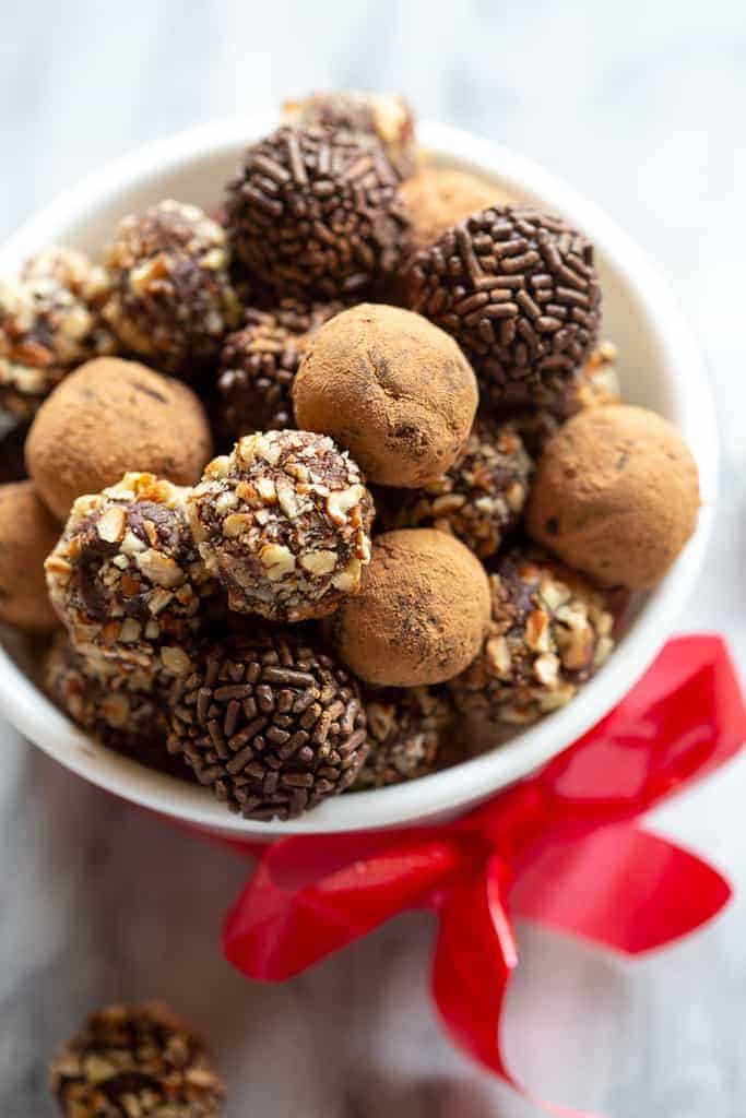 A bowl of chocolate truffles coated with cocoa powder, chopped nuts and chocolate sprinkles.