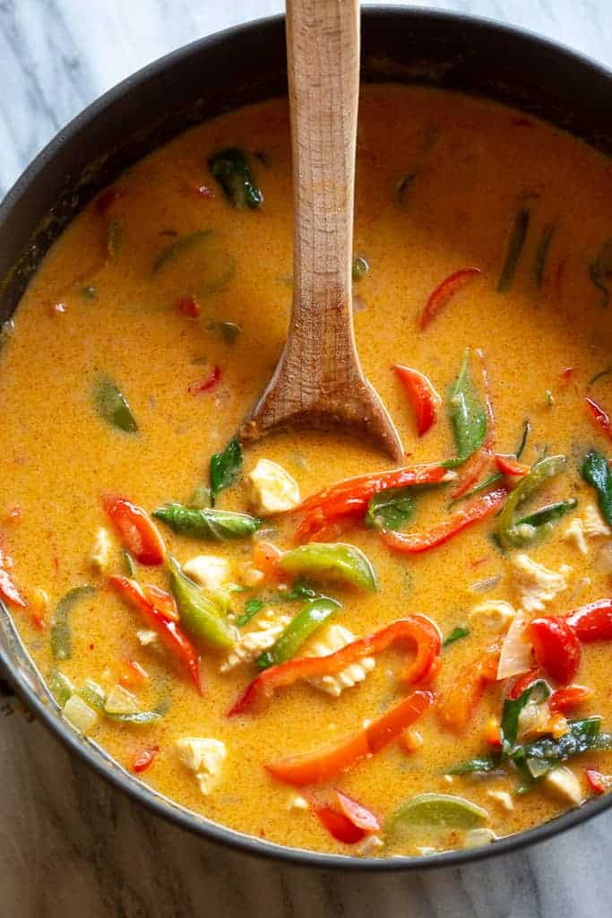 Panang curry with bell peppers, chicken and basil, in a pot with a wooden spoon.