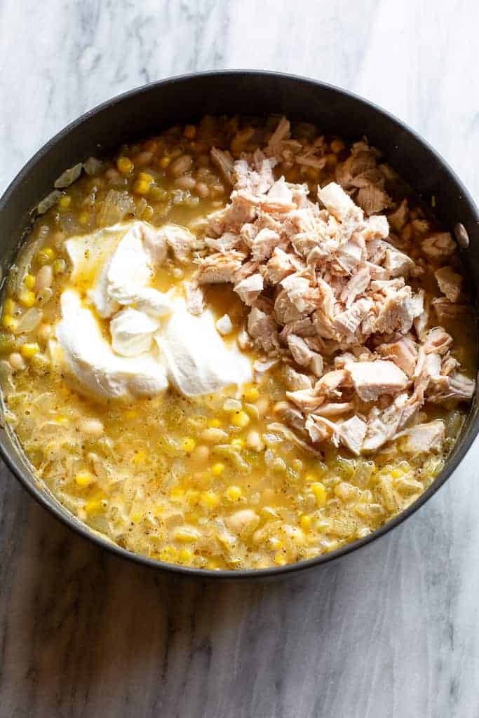 Sour cream and shredded cooked chicken added to a pot of white chicken chili.