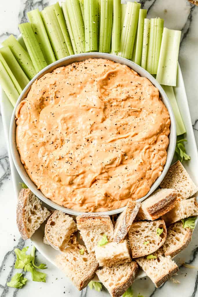 Buffalo chicken dip served in a bowl, with celery sticks and bread cubes on the side.